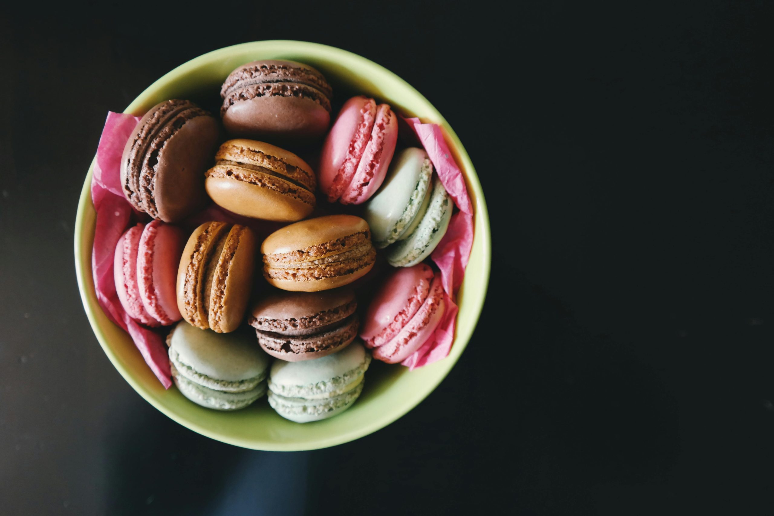 A vibrant assortment of macarons in a green bowl, perfect for dessert themes.