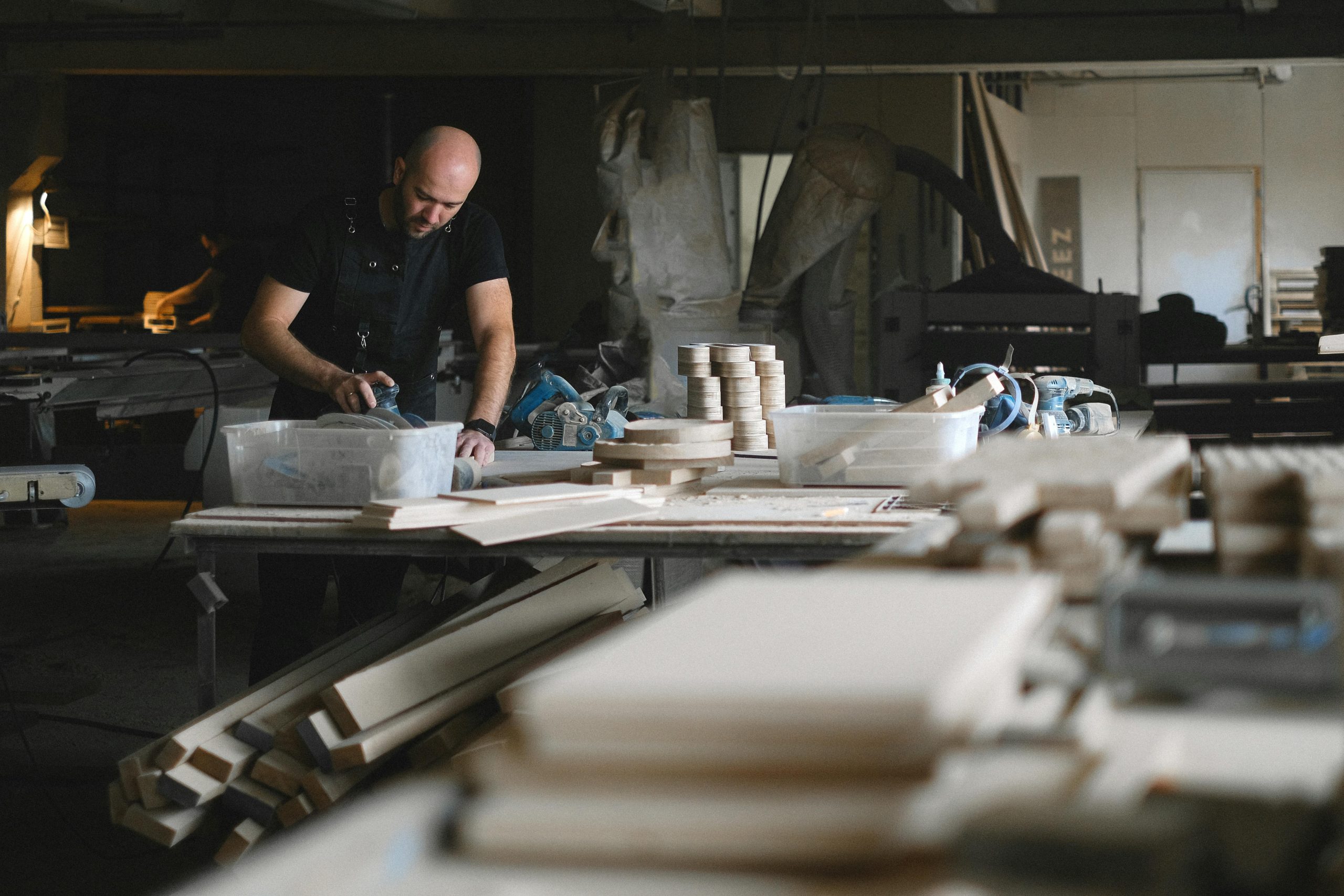 A craftsman focused on woodworking in a busy indoor workshop with tools and timber.