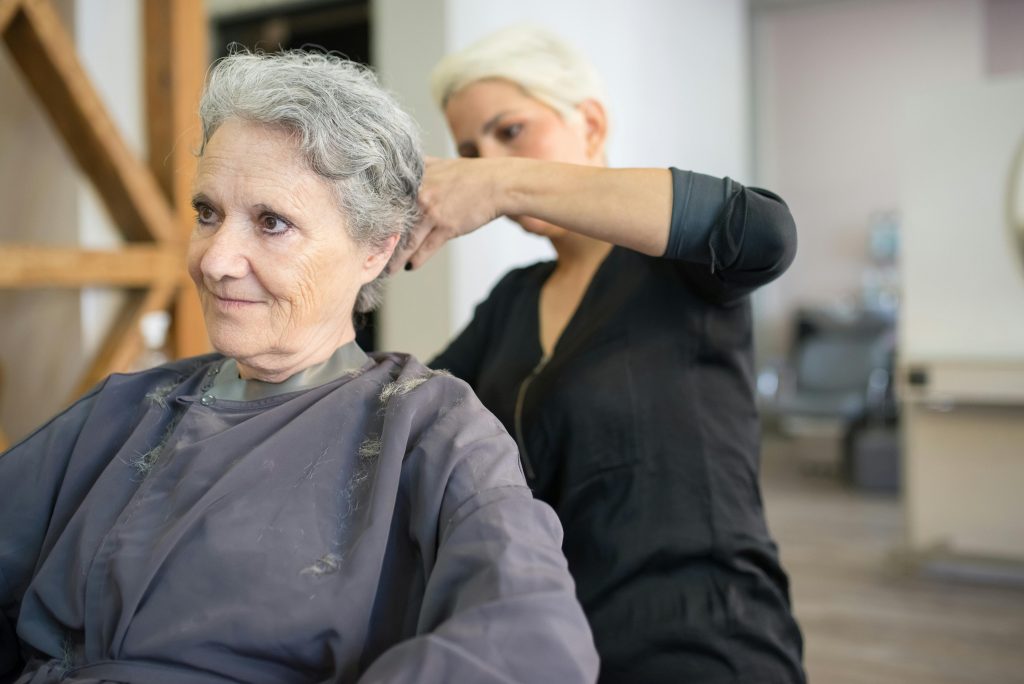 A senior woman receives a haircut at a salon, showcasing a skilled hairstylist in action.